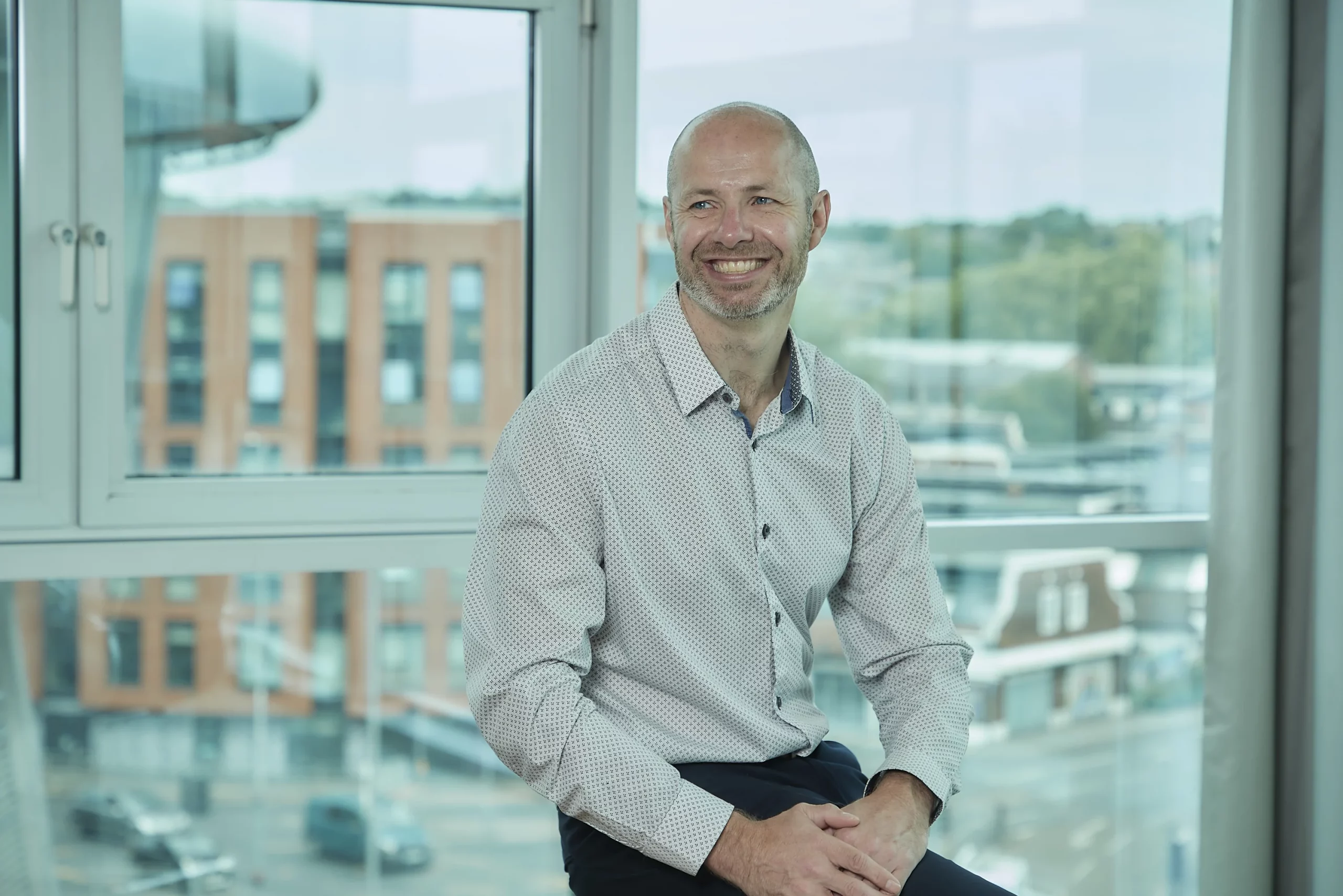 David Laws, founder of Responsive Analytix, sitting by a window with a city view behind him